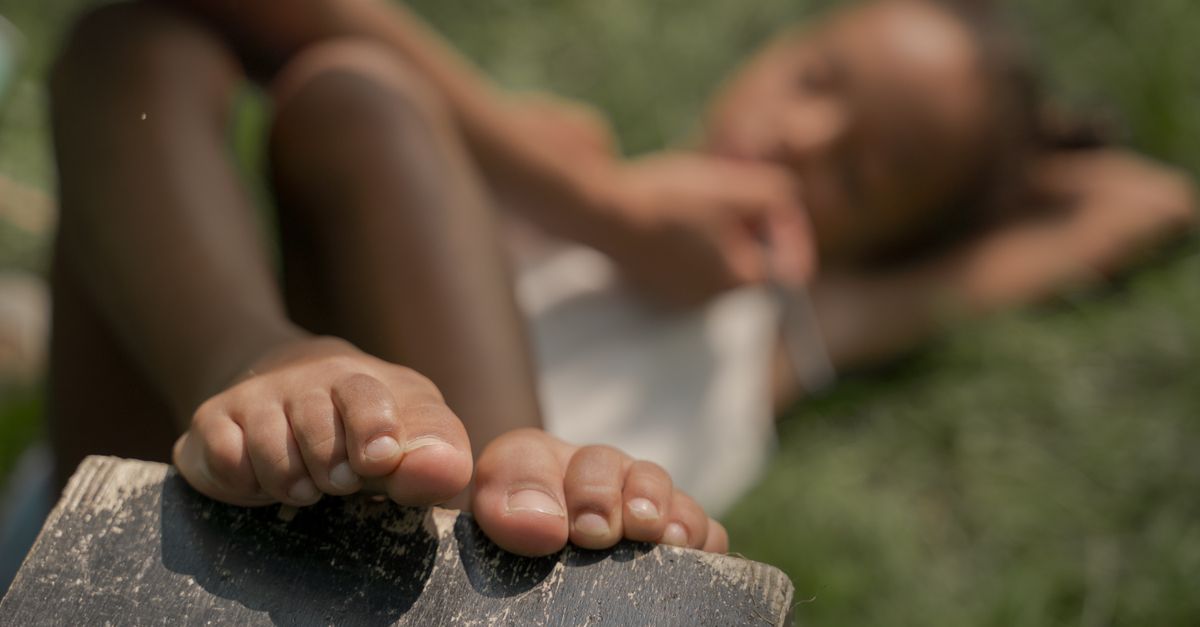 A child laying on the grass, enjoying a sunny summer day with a focus on bare feet.